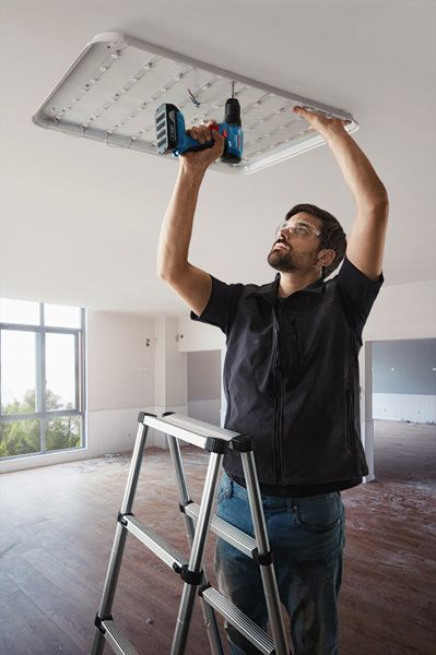 En person iført sikkerhedsudstyr installerer en loftslampe ved hjælp af en boremaskine.